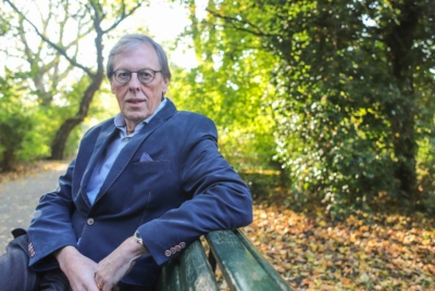 meneer met bril zit op een bankje in een groene omgeving